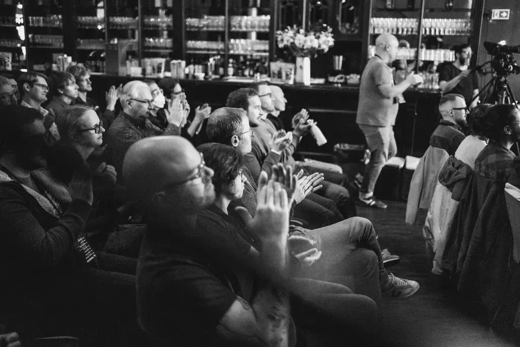 A photos showing the audience of the event, taken from the right of the audience and you can see people applauding and smiling.