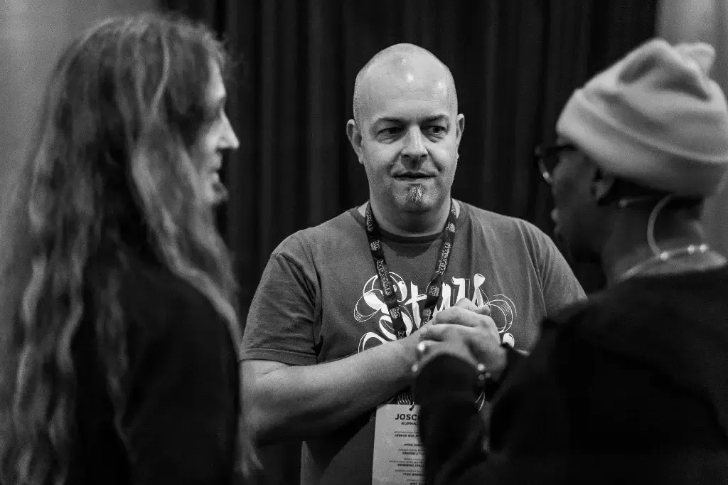 A photo on which you see three people. Marc Thiele blurry on the left, Joschi Kuphal in the center and in focus and a blurred Adah Parris on the right.