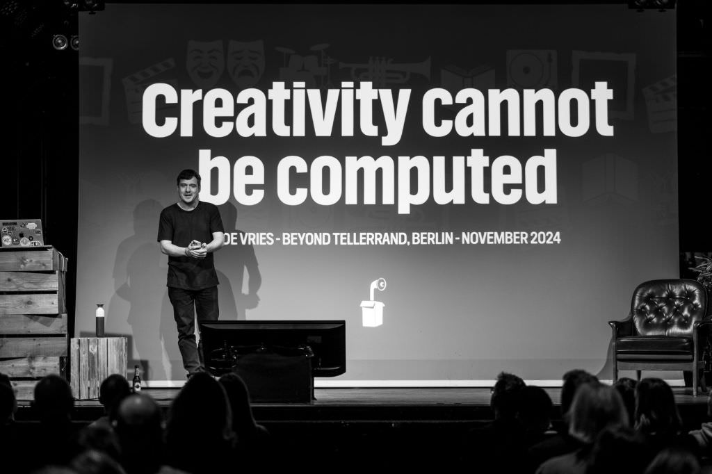 A black and white photo of Hidde de Vries on stage at beyond tellerrand in Berlin. The slide in his back shows the title of his talk in large letters and says “Creativity cannot be Computed”