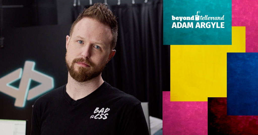 A photo of Adam Argyle looking into the camera. He stands in front of a blurry background and his t-shirt says “Bad @CSS”