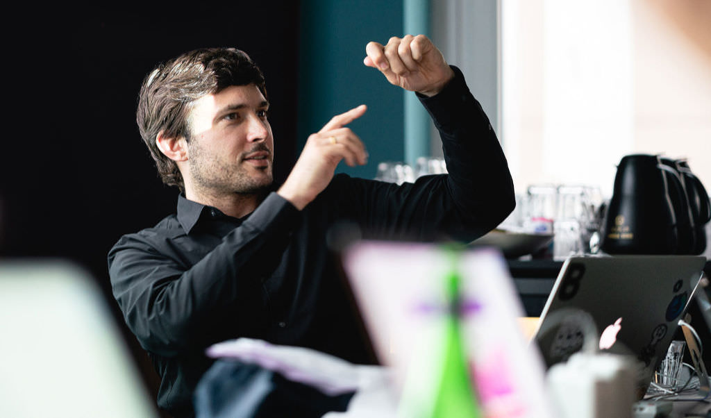 A photo of Matthias Ott teaching a workshop. He is caught, making a gesture to show the size of something. Matthias wears a black shirt.