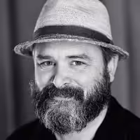 A portrait photo of Vasilis van Gemert. He has a longer beard, partly grey and black. On this photo he wears a head and smiles friendly into the camera..